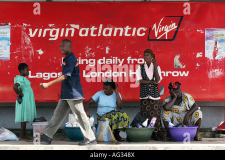 Un homme marche passé, les femmes qui vendent des marchandises à l'avant d'un Virgin Airlines poster Lagos, Nigéria Banque D'Images