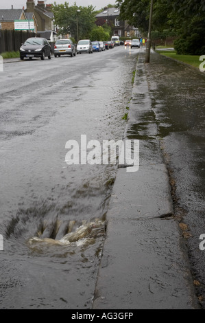 L'eau courant le long d'une route dans une grille de débordement par le trottoir. Banque D'Images