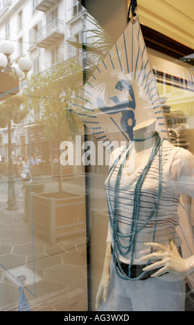 Mannequin sans tête dans une vitrine habillé en blanc avec des chaînes de perles de couleur et d'image double relection d'une rue Banque D'Images