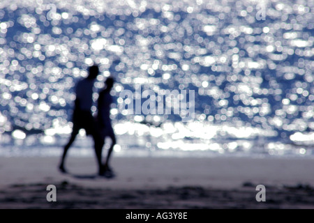 Couple walking along beach silhouetté contre mer réflexions floues soft focus Banque D'Images