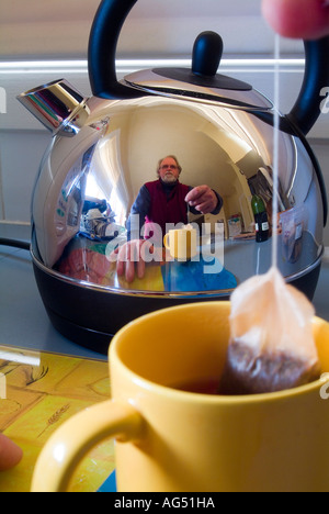 Homme faisant une tasse de thé reflété dans une bouilloire électrique en acier inoxydable brillant Banque D'Images