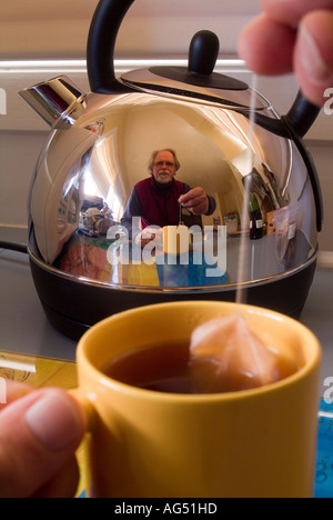 Homme faisant une tasse de thé reflété dans une bouilloire électrique en acier inoxydable brillant Banque D'Images