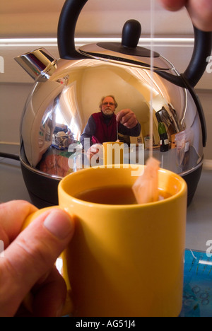 Homme faisant une tasse de thé reflété dans une bouilloire électrique en acier inoxydable brillant Banque D'Images