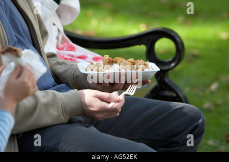 Close up of père assis avec deux enfants de manger à emporter repas chinois et crêpes à l'extérieur, sur un banc de parc Banque D'Images