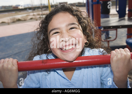 Dix ans, fille accroché à bar sur cour de l'école, grand sourire à pleines dents lumineuses Banque D'Images