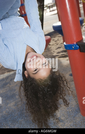 Dix ans, fille hispanique tête en bas sur l'aire de jeux, smiling Banque D'Images
