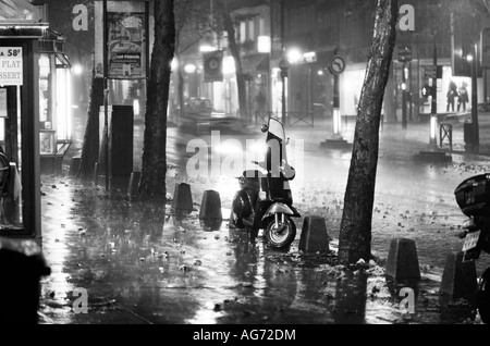 Un scooter garé sur un trottoir sur le Boulevard Saint Michel à Paris pendant un orage dans la nuit Banque D'Images