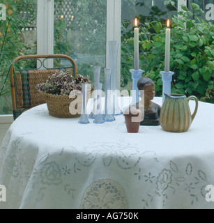 Les chandeliers en verre bleu et des vases avec panier et petite statue sur nappe blanche dans la véranda salle à manger Banque D'Images