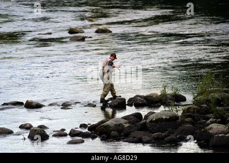 Pêcheur de mouche marche sur des pierres glissantes à fleuve , Finlande Banque D'Images