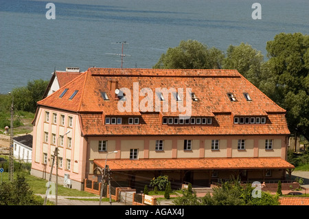 Grand bâtiment carrelé rouge avec lucarnes et puits de lumière à Frombork, Warmia, Pologne, situé près de l'eau et entouré d'arbres. Banque D'Images