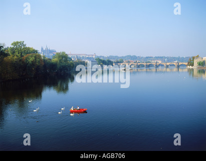 Alimentation deux cygnes de chaloupe rouge sur la Vltava avec le Pont Charles à Prague Banque D'Images