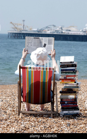 Lecture d'été grave pour un homme avec une pile de livres techniques sur la plage de Brighton avec la jetée de l'arrière-plan Banque D'Images