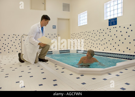 Thérapeute physique in lab coat monitoring middle aged male patient in pool Banque D'Images