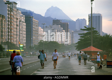 Les personnes prenant matin promenade le long de la plage de Copacabana à Rio de Janeiro au Brésil avec le célèbre mont du Pain de Sucre pic au-dessus Banque D'Images