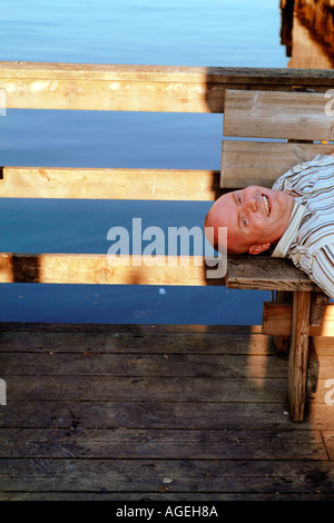 Un homme heureux portant sur un banc en bois par la mer, smiling Banque D'Images