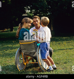 Petit garçon donnant des fleurs pour femme handicapée en fauteuil roulant : et l'homme dans le jardin Banque D'Images