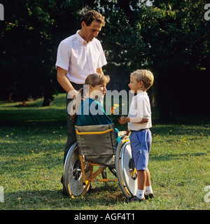 Petit garçon donnant des fleurs pour femme handicapée en fauteuil roulant : et l'homme dans le jardin Banque D'Images