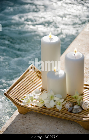 Allumé des bougies pilier sur plateau avec les orchidées blanches à côté piscine Banque D'Images