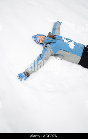 Smiling attractive young woman wearing blue vêtements de ski se trouvant dans la neige avec les yeux fermés making snow angel Banque D'Images