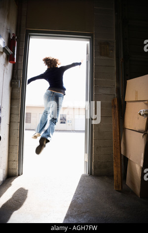 Femme courir et sauter à travers la porte ouverte d'un bâtiment à l'extérieur ensoleillé Banque D'Images