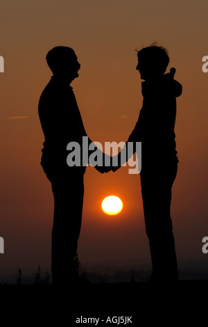 Un couple qui se profile se tenant la main avec un soleil couchant en arrière-plan Banque D'Images