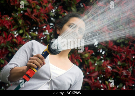 Jeune femme d'arroser son jardin avec un tuyau flexible Banque D'Images