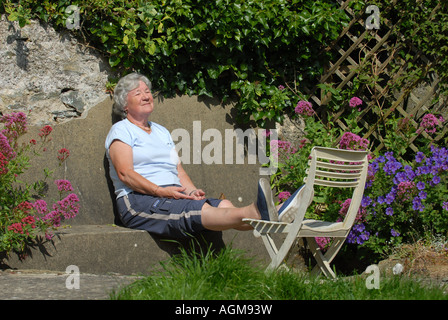 Un retraité femme bénéficie d'un bain de soleil dans son jardin à l'AUTOMNE LA RETRAITE RE ANS.UK Banque D'Images