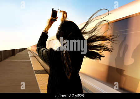 Femme travaille sur PDA téléphone cellulaire comme un train de banlieue à proximité des vitesses soufflant ses cheveux longs dans l'appareil photo Banque D'Images