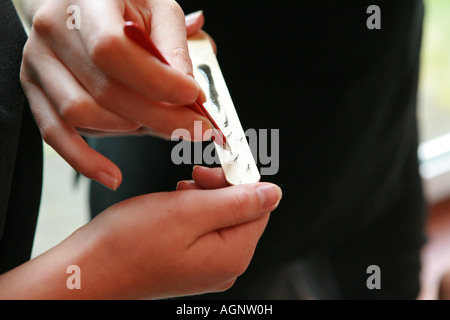 Esthéticiennes tenir et soulever de faux cils de l'œil avec des brucelles à partir d'une bande de papier avant de les appliquer à un client dans un salon de beauté. Banque D'Images