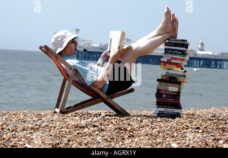 Lecture d'été grave pour un homme avec une pile de livres techniques sur la plage de Brighton avec la jetée de l'arrière-plan Banque D'Images