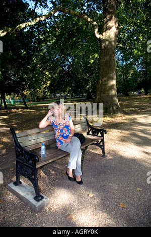 Une jeune femme dans la vingtaine. Assis sur un banc de parc tout en parlant au téléphone Banque D'Images