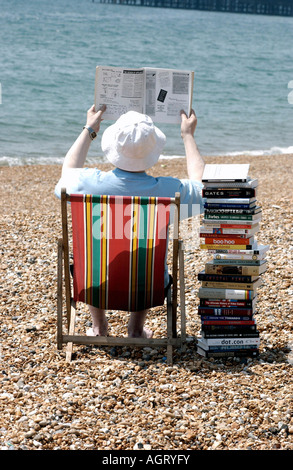 Lecture d'été grave pour un homme avec une pile de livres techniques sur la plage de Brighton avec la jetée de l'arrière-plan Banque D'Images