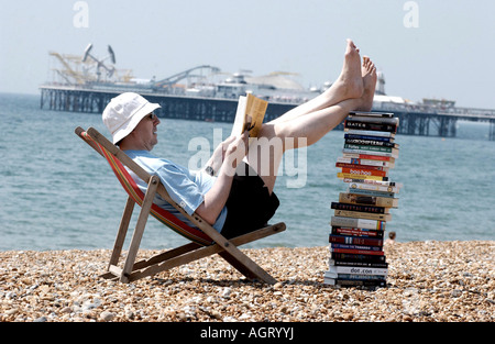 Lecture d'été grave pour un homme avec une pile de livres techniques sur la plage de Brighton avec la jetée de l'arrière-plan Banque D'Images