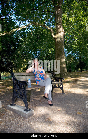 Une jeune femme dans la vingtaine. Assis sur un banc de parc tout en parlant au téléphone Banque D'Images