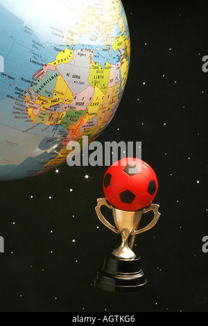 Petite tasse en métal rouge et noir avec boule en caoutchouc de soccer ou de football et sport world globe contre fond noir étoilé Banque D'Images