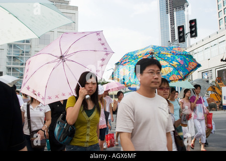 Les jeunes de Shanghai se protéger de le soleil avec des parapluies lorsqu'ils traversent la route à la jonction à côté de la Place du Peuple Banque D'Images