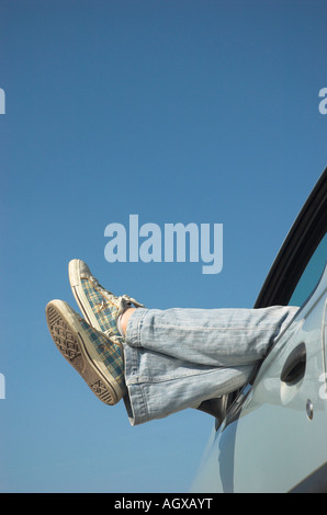 Jeune femme jambes dépassant du pare-brise de voiture Banque D'Images