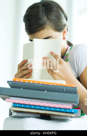 Teen girl avec pile de devoirs, de se cacher derrière la face book, portrait Banque D'Images