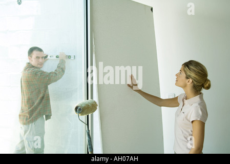 Man holding niveau contre mur et woman putting hand against wall board Banque D'Images