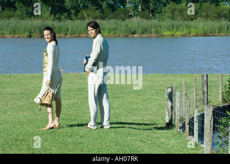 Couple outdoors, woman holding purse et man holding laptop, à la fois sur les épaules, smiling at camera Banque D'Images