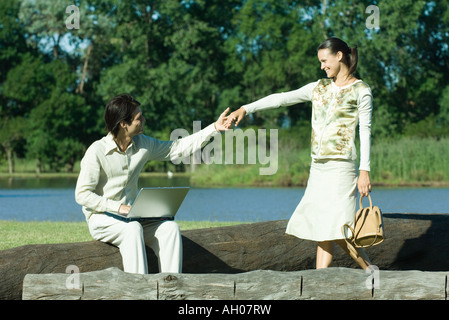 Homme assis sur tronc d'arbre avec un ordinateur portable sur les genoux, pour atteindre la main de femme comme elle approche Banque D'Images