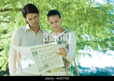 Couple standing outdoors, reading newspaper Banque D'Images