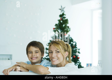 Garçon et la mère sur canapé, arbre de Noël en arrière-plan, smiling at camera Banque D'Images