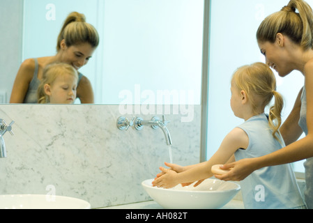 Woman helping petite fille se laver les mains au lavabo de la salle de bains Banque D'Images