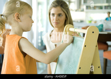 Femme regardant petite fille dessiner on chalkboard Banque D'Images