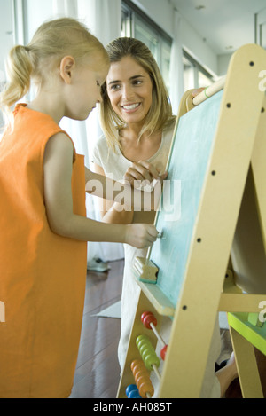 Femme regardant petite fille dessiner on chalkboard Banque D'Images