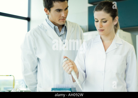 Femme lab worker holding dropper, regarder son collègue masculin Banque D'Images