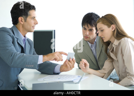 En fonction de l'homme assis en face de jeune couple, pointant à la calculatrice Banque D'Images