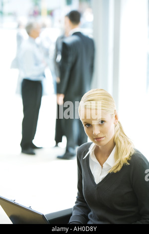 Young businesswoman using laptop, looking at camera, associés en arrière-plan Banque D'Images