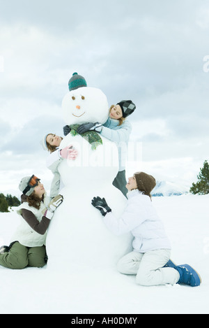 Jeunes amis embracing snowman, smiling, pleine longueur Banque D'Images